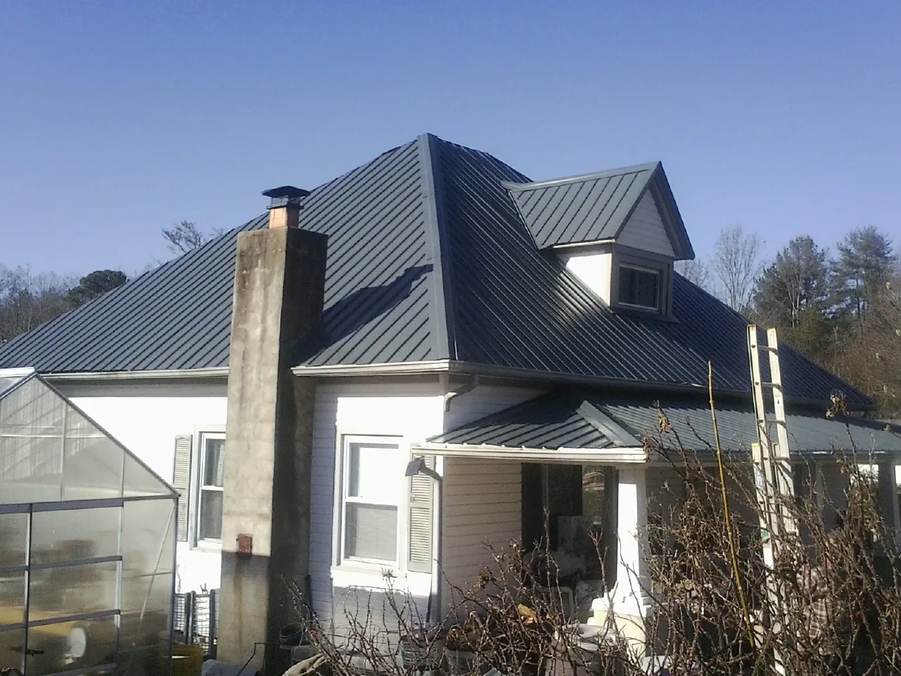 Dark blue standing seam metal roof on a white farmhouse with dormer — Slate & Tile Roof Repair by Roofing Brothers in Klemme
