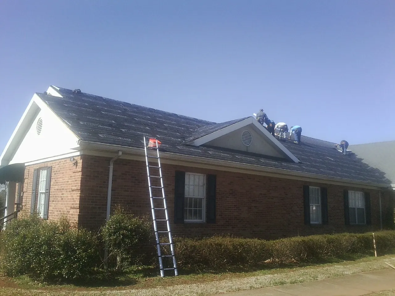 Crew tearing shingles off a brick ranch roof with a ladder set — Emergency Roof Repair work by our crew in Klemme