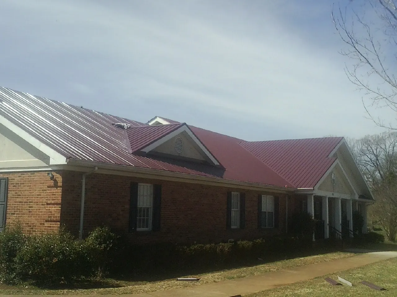 Red metal roof with gabled entries on a long brick building, from a Hail Damage Roof Repair job in Klemme