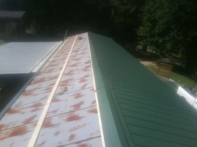 Old rusted panels beside newly installed green metal roofing — Wind Damage Roof Repair by Roofing Brothers in Klemme
