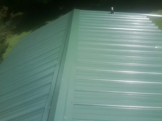 New green metal panels meeting at the ridge of a roof — Flat Roof Repair work by our crew in Klemme