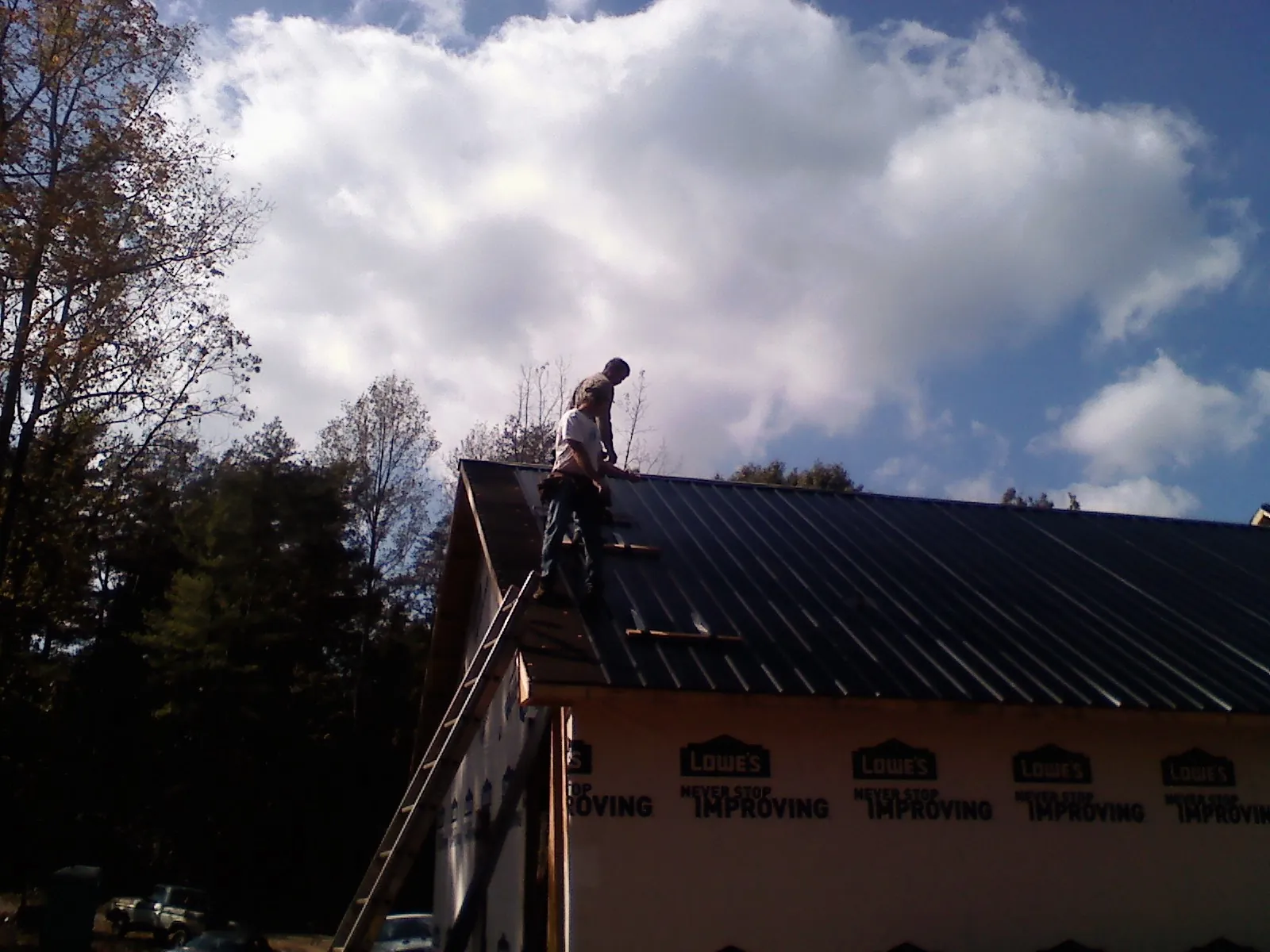 Roofer fastening dark metal panels high against a cloudy sky, from a Roof Inspection job in Klemme