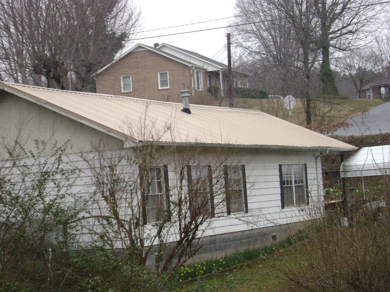 Tan metal roof on a white sided house set into a hillside — Commercial Roofing by Roofing Brothers in Klemme