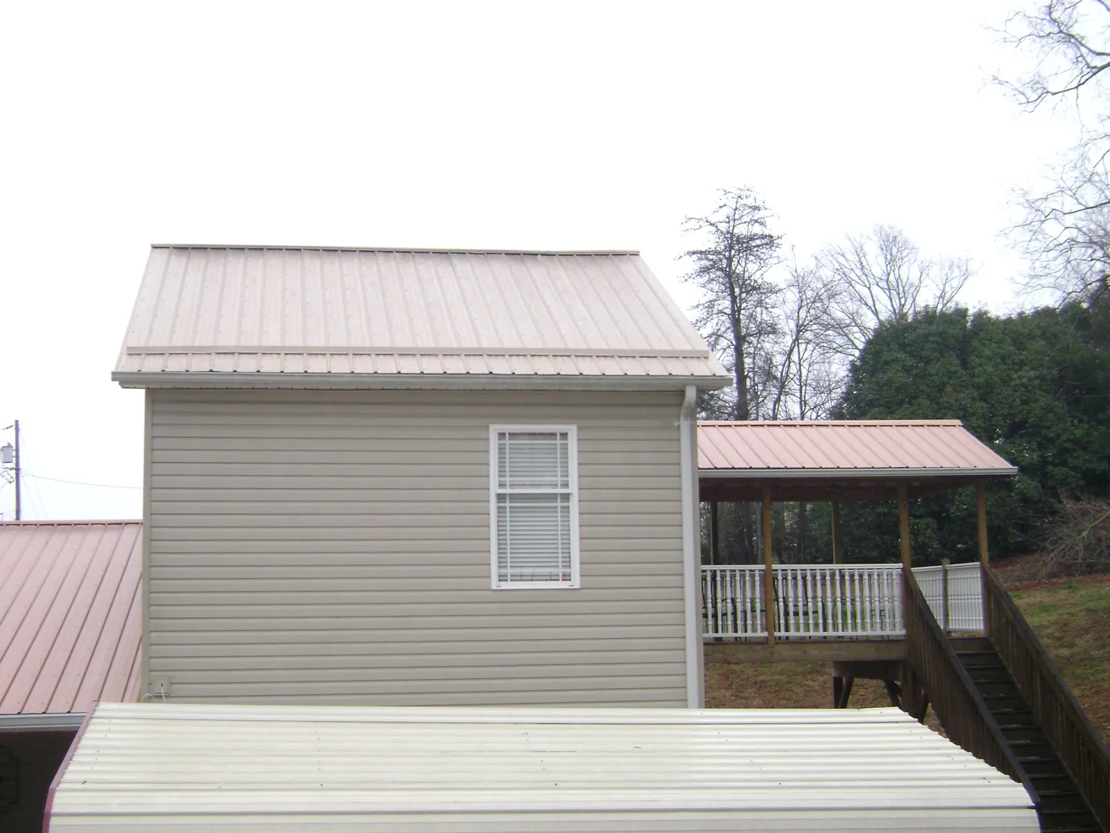 Tan metal roofs on a two story addition and attached porch, from a Roof Replacement job in Klemme