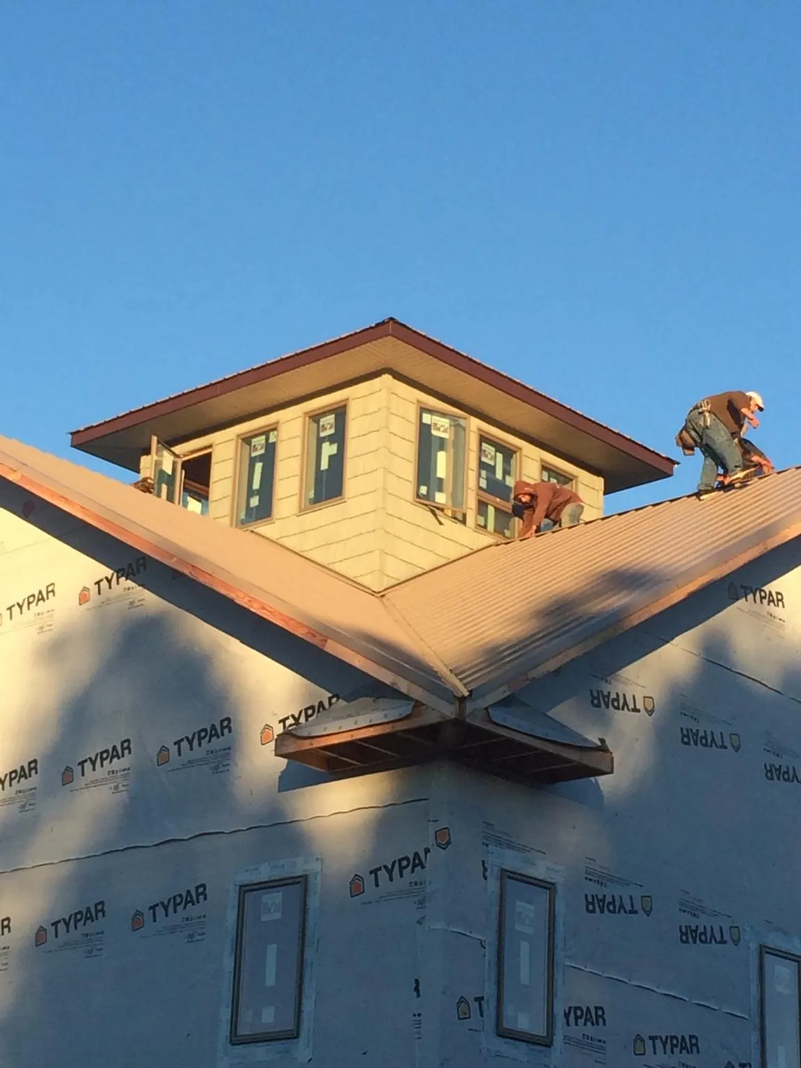 Roofers working around a rooftop cupola on a new metal roof at sunset — Roof Waterproofing in Klemme by Roofing Brothers